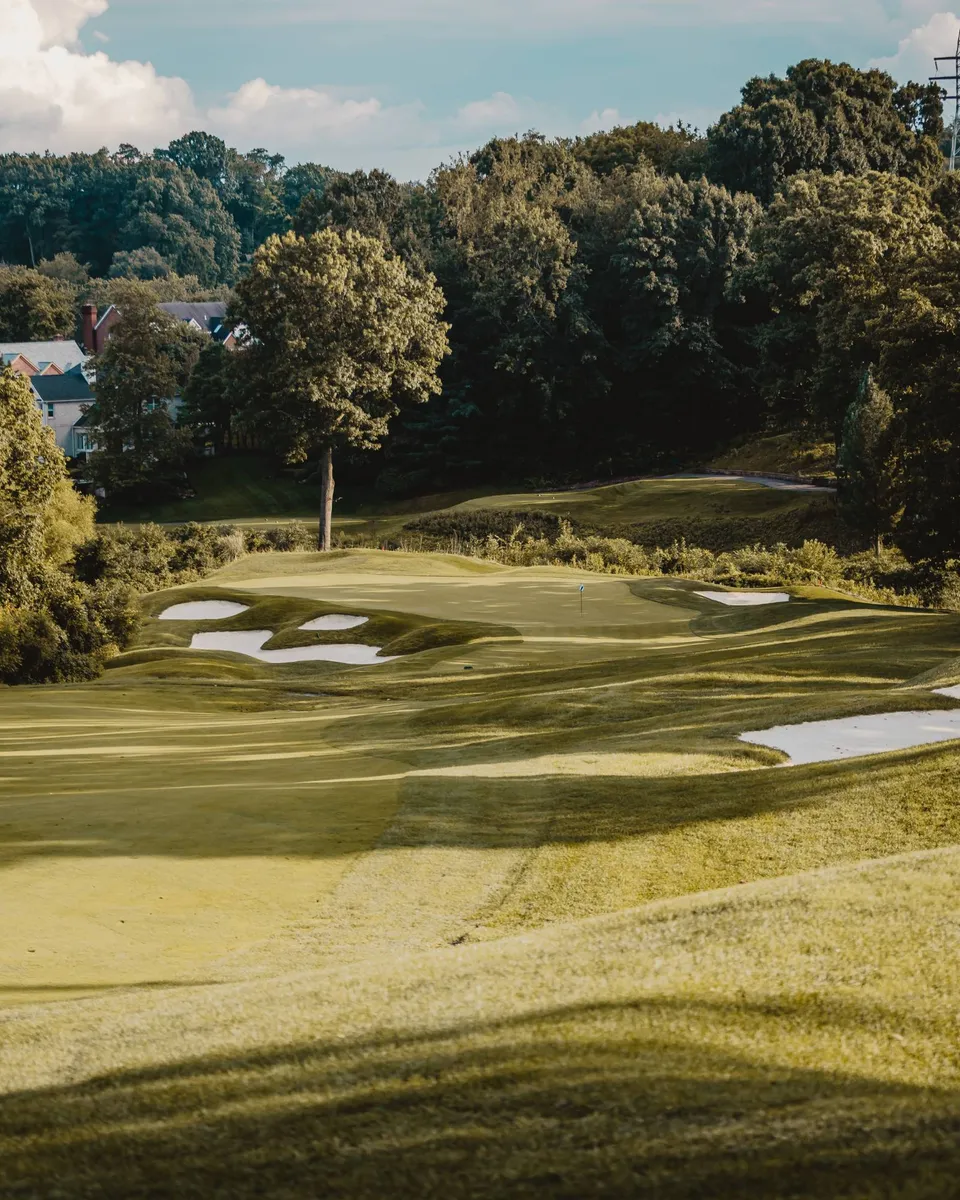 Golf course green framed by bunkers and mature trees