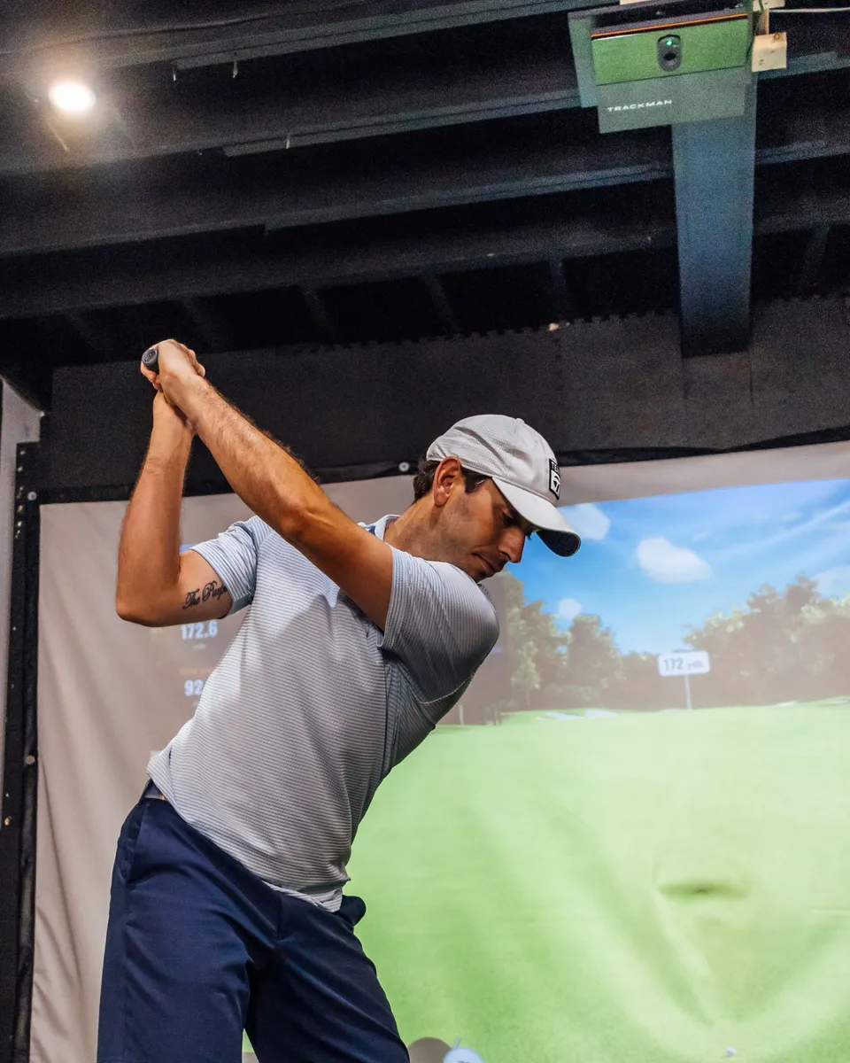 Golfer at the top of the backswing in a TrackMan simulator bay
