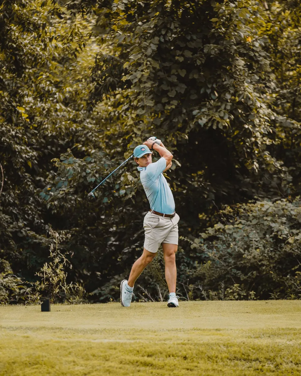 Golfer holding the finish of a drive on a tree-lined tee