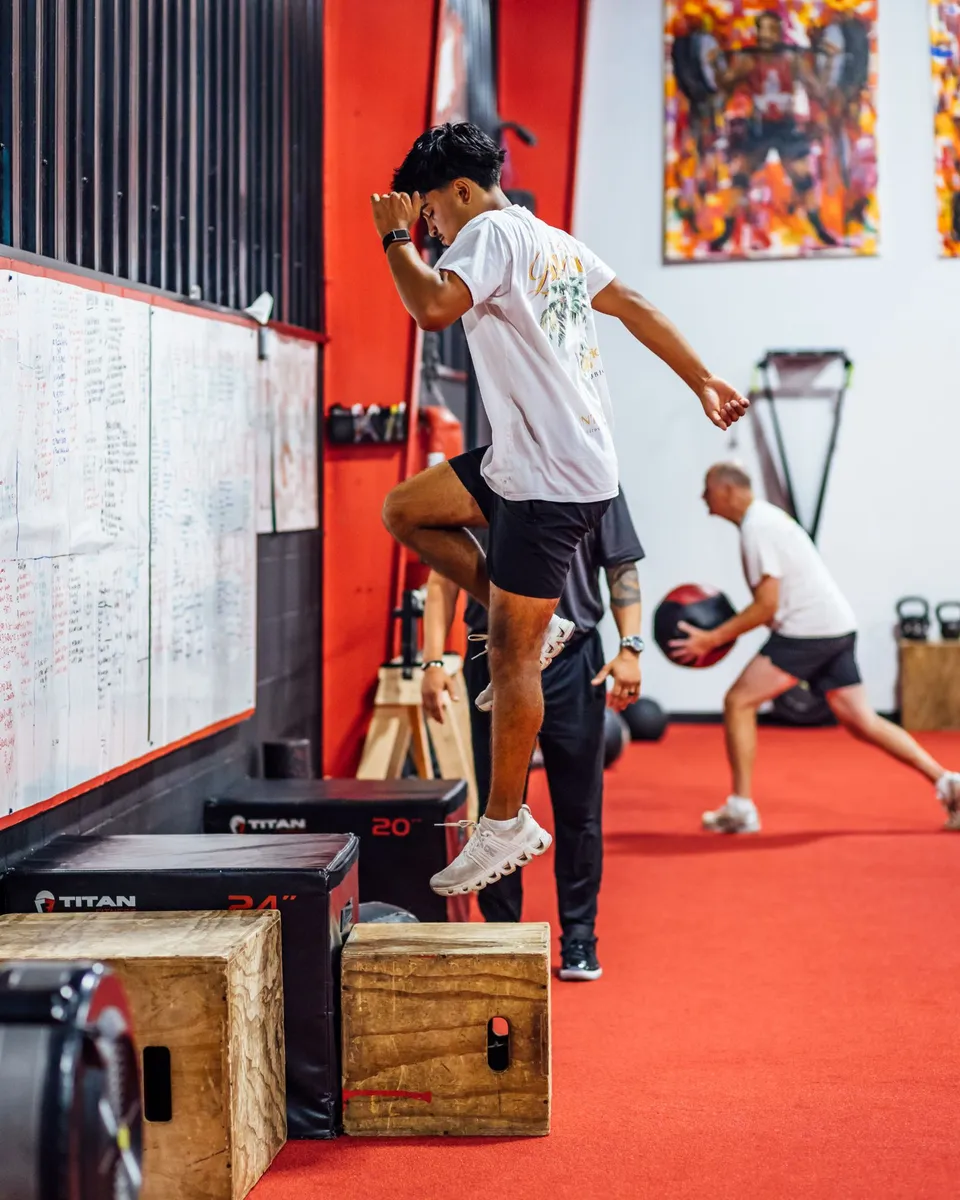 Golfer doing a box jump with Tim Merolillo, owner and head trainer at Elite Custom Fitness, spotting
