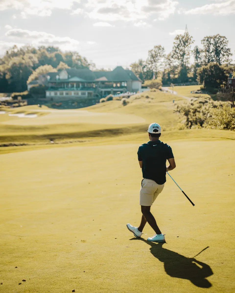 Golfer walking the course at a local private golf club with the clubhouse in the distance